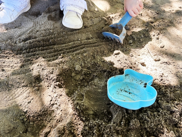 イヤイヤ期の子どもと砂場で遊ぶ光景